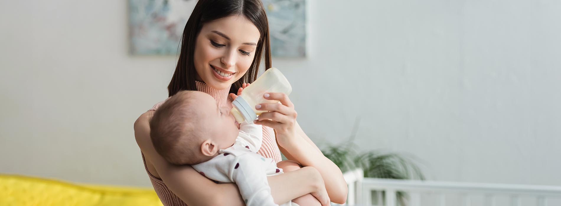 A woman holding a baby while feeding herself with a spoon, captured from behind.