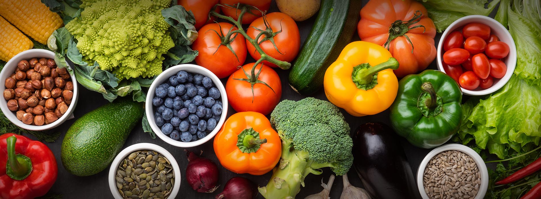 The image displays a colorful assortment of fresh fruits and vegetables arranged in a circular pattern around a central display of broccoli, with various types of produce including tomatoes, peppers, cucumbers, carrots, and leafy greens showcased in bowls.