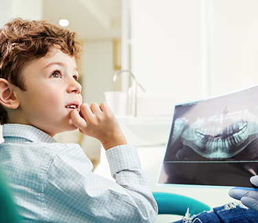 A young boy examining a dental X-ray with a surprised expression while sitting in a dentist s chair.